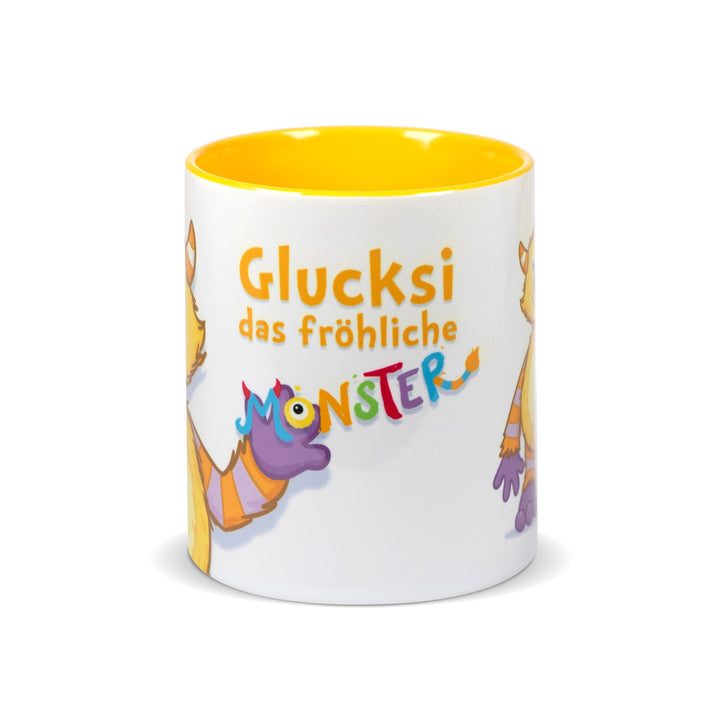 Weiße Keramiktasse mit gelbem Innenrand und der Aufschrift „Glucksi das fröhliche Monster“ in bunter, verspielter Schrift.